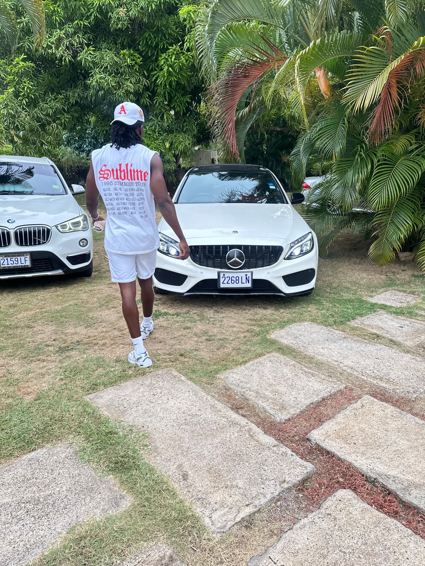 Musa X outside, walking past a white Mercedes